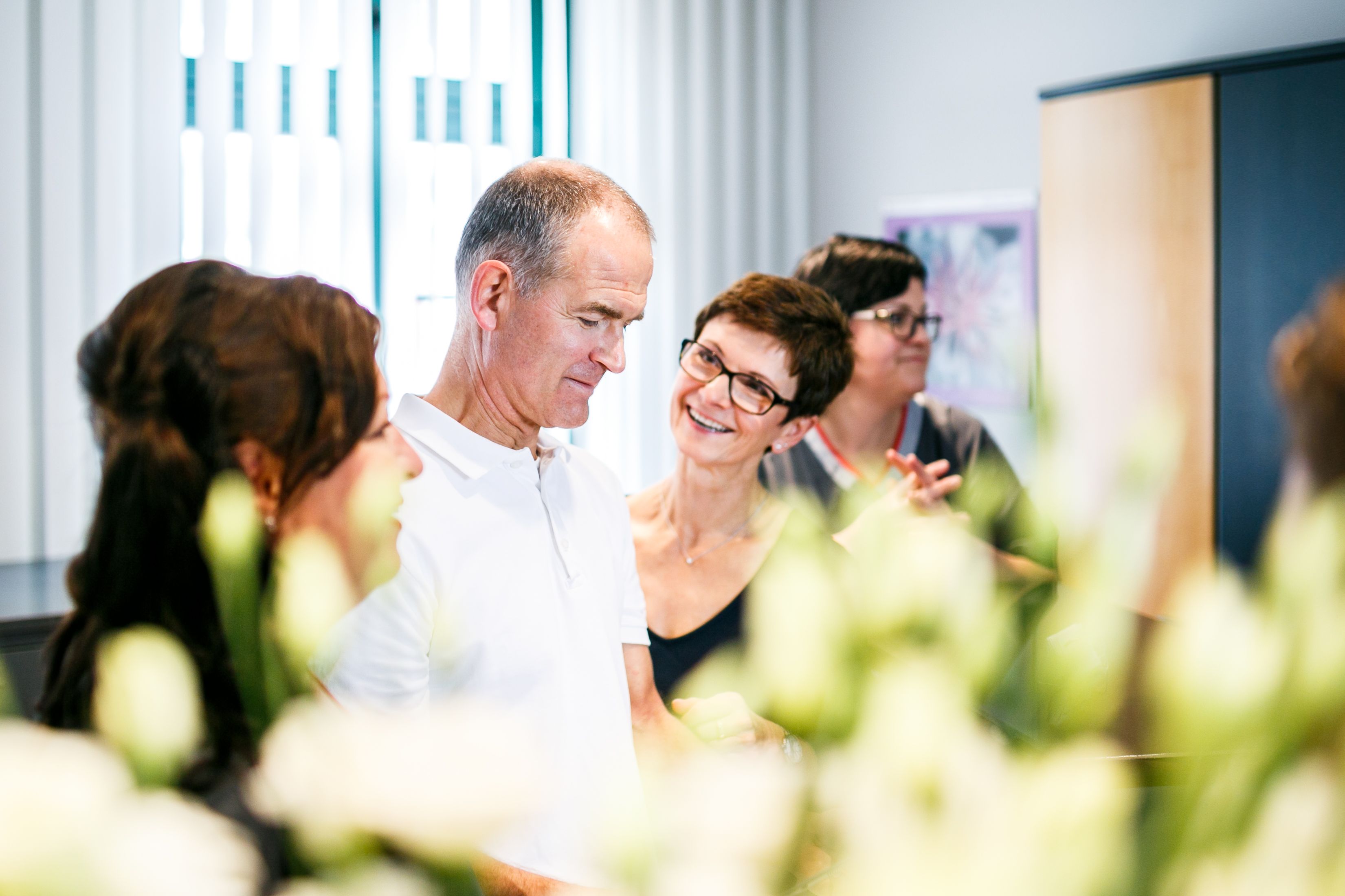 Praxisteam im Gespräch, im Vordergrund Blumen, helles Licht