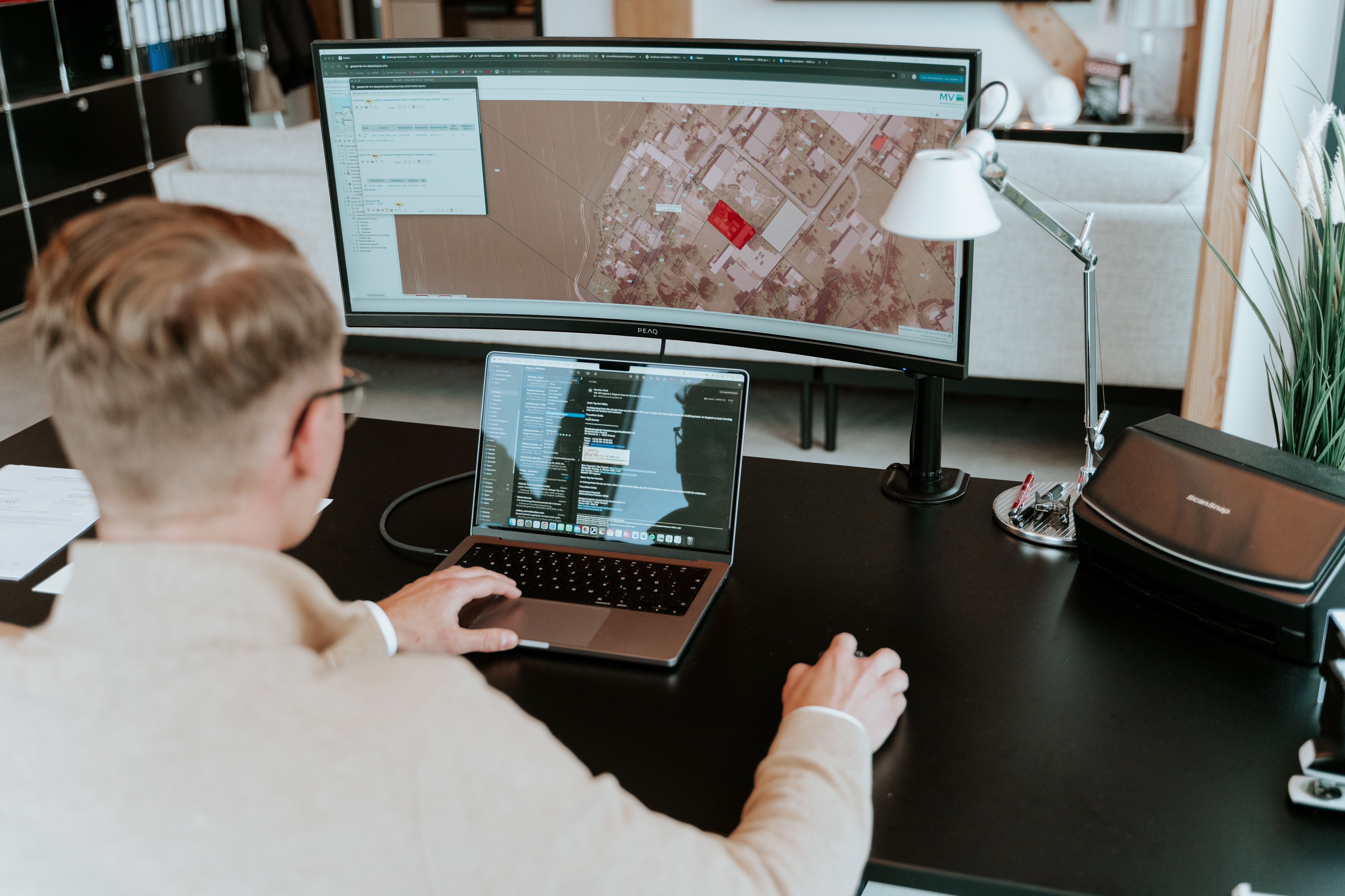 Person arbeitet am Schreibtisch mit Laptop und großem Monitor mit Karte