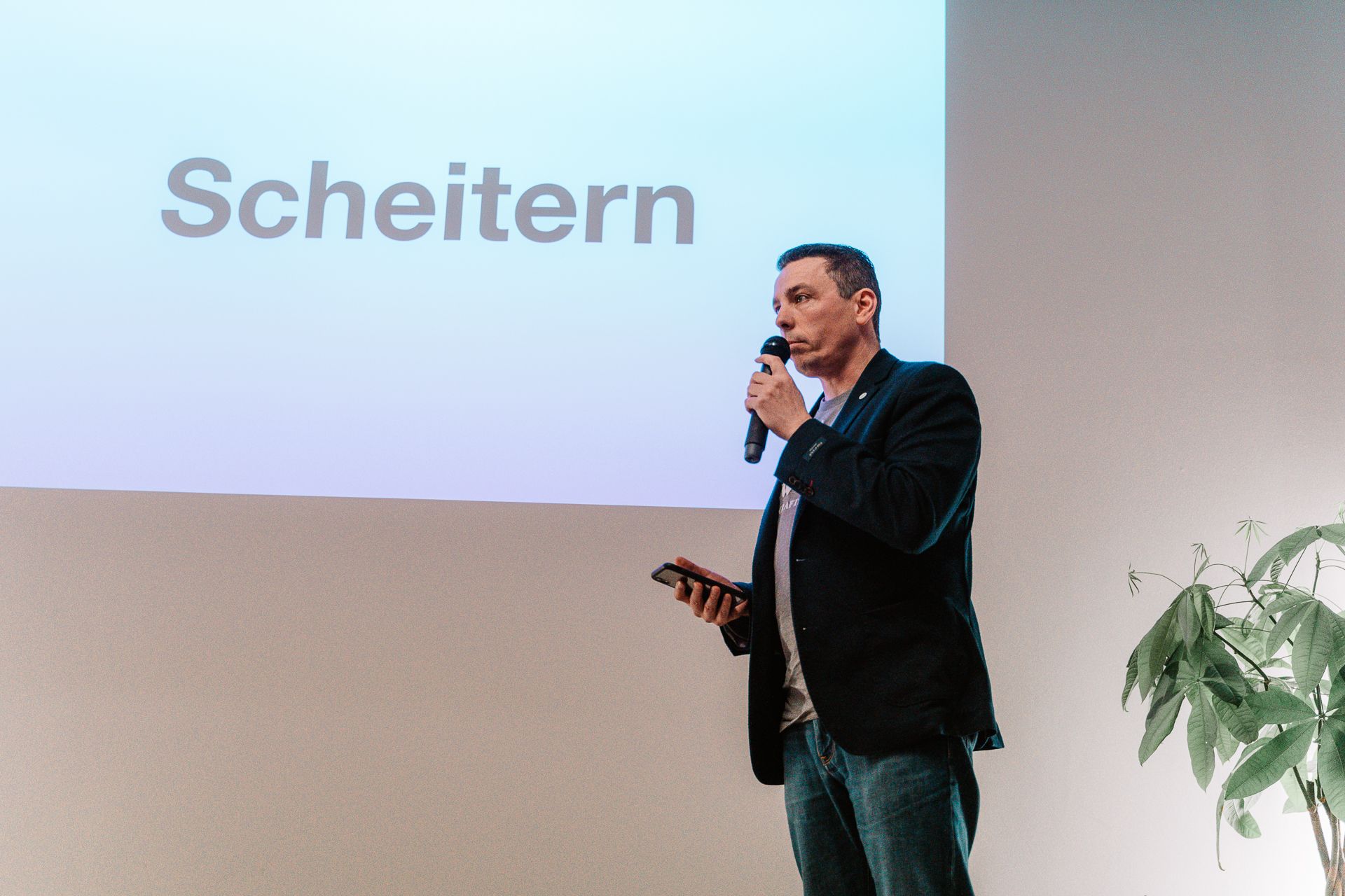 Redner mit Mikrofon vor einer Leinwand in einem hellen Raum