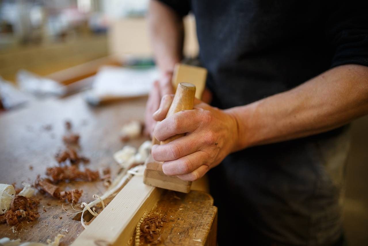 Hände führen einen Hobel über ein Werkstück aus Holz