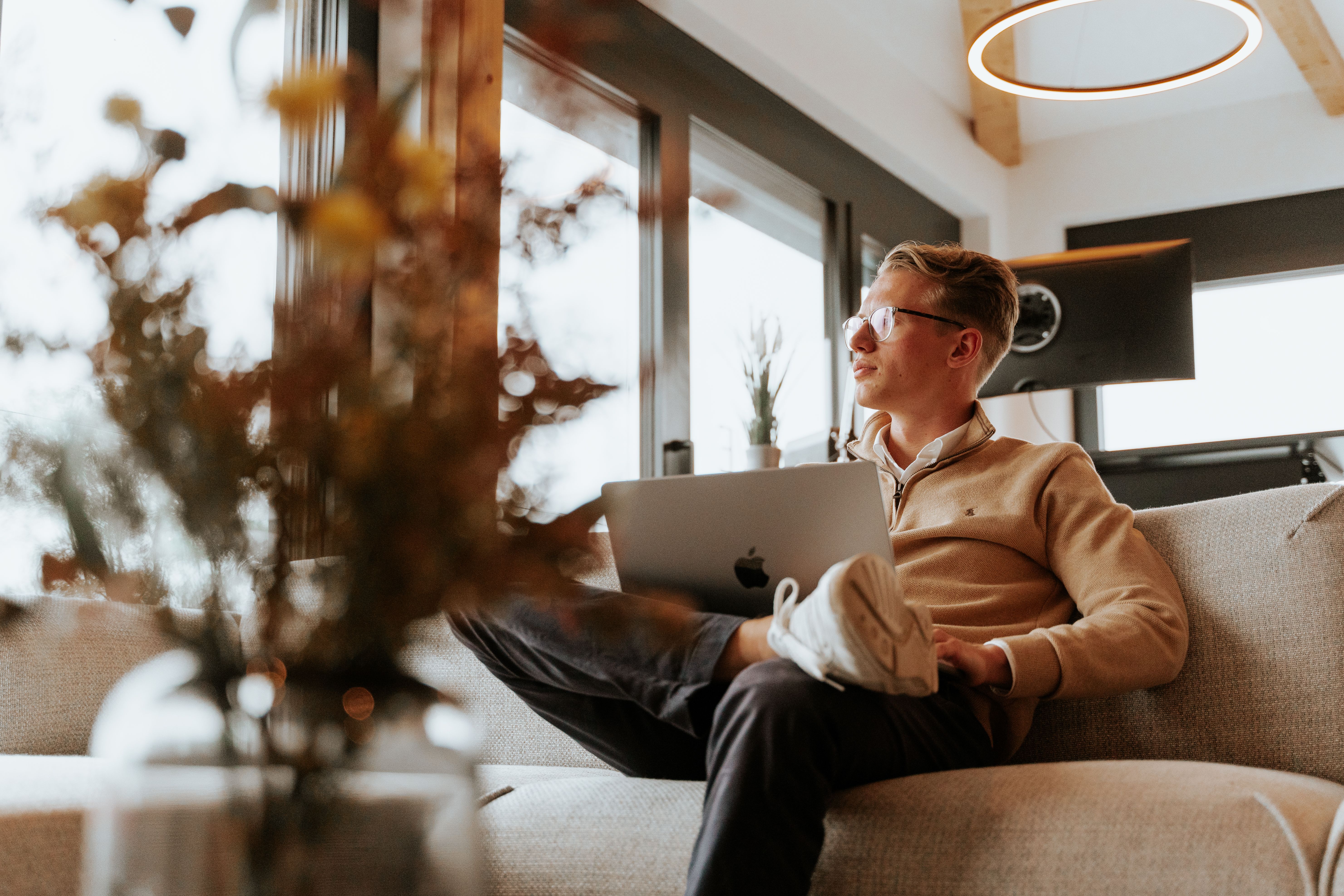 Mann mit Laptop sitzt auf einem Sofa am Fenster, Tageslicht