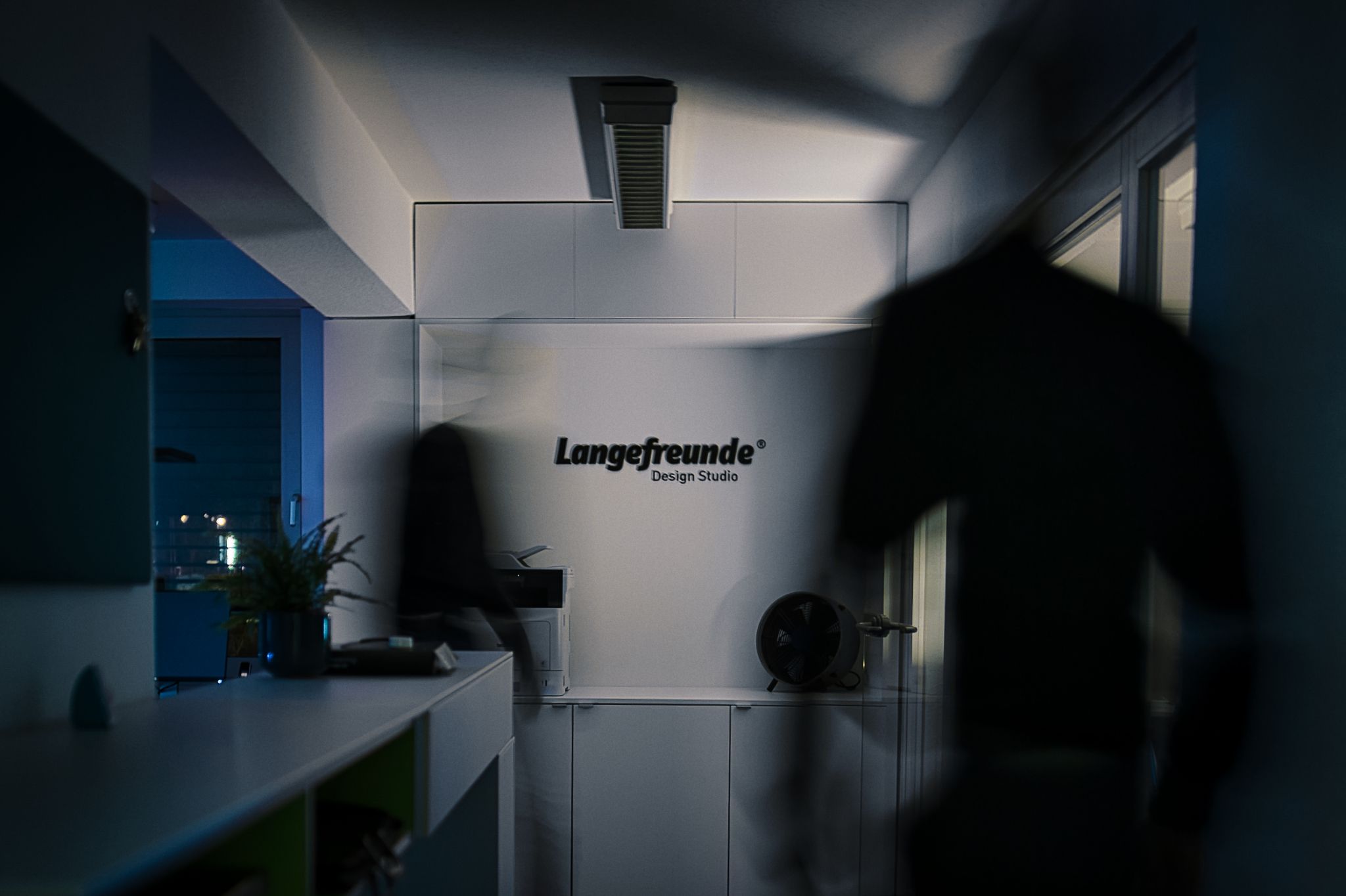 Moderner Büroraum mit Logo an der Wand, bewegte Silhouette, kühles Licht