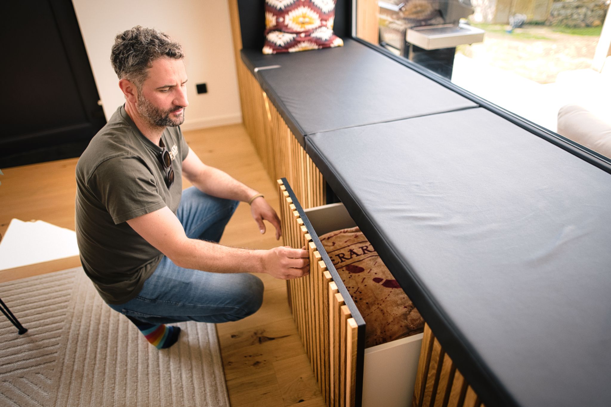Mann hockt vor einem Holzschrank in einem hellen Wohnraum