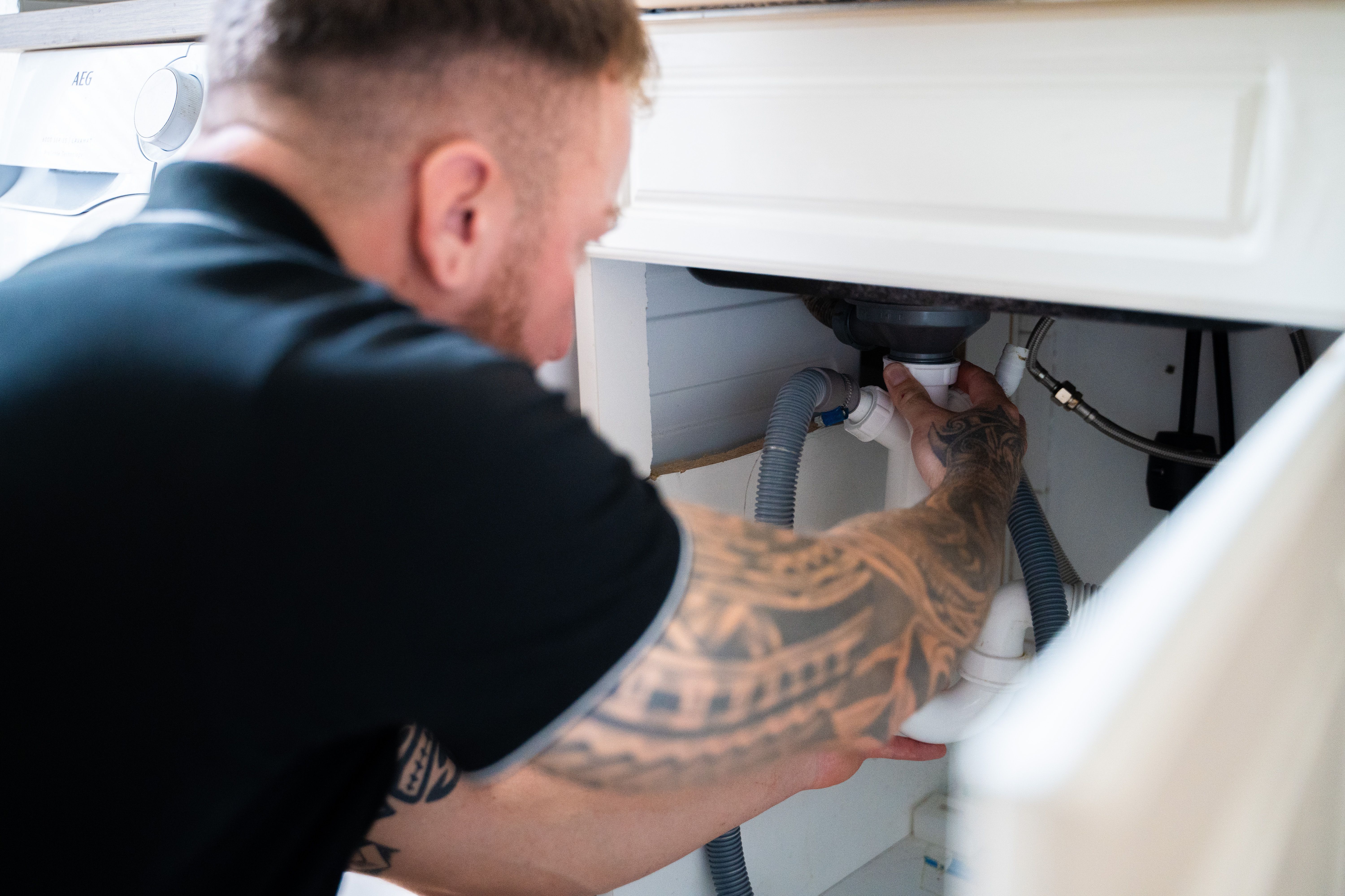 Handwerker mit Tattoos arbeitet an einem Siphon unter einem Waschbecken