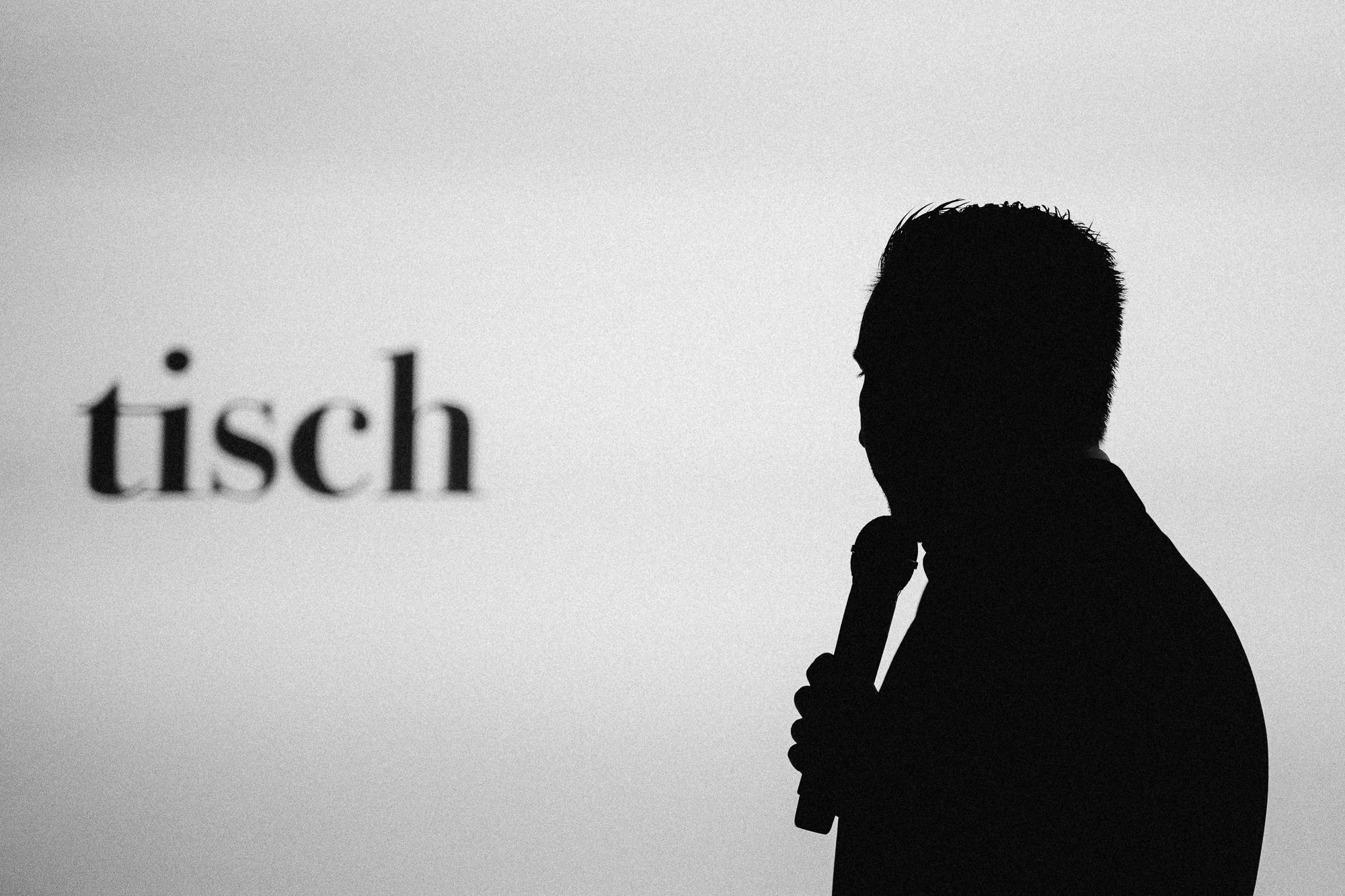 Silhouette eines Redners mit Mikrofon vor heller Wand