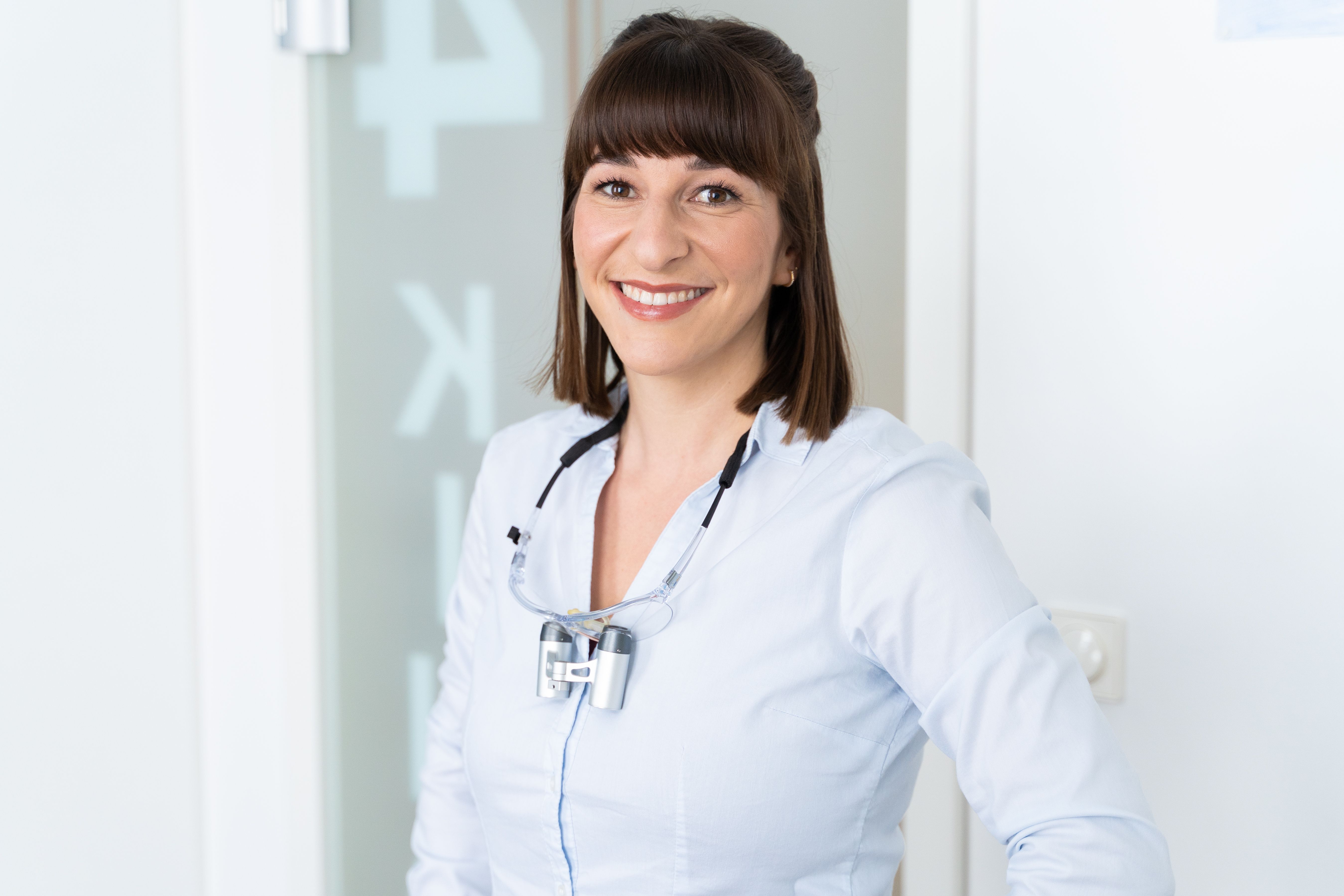 Lächelnde Zahnärztin mit Lupenbrille in einer hellen Praxis
