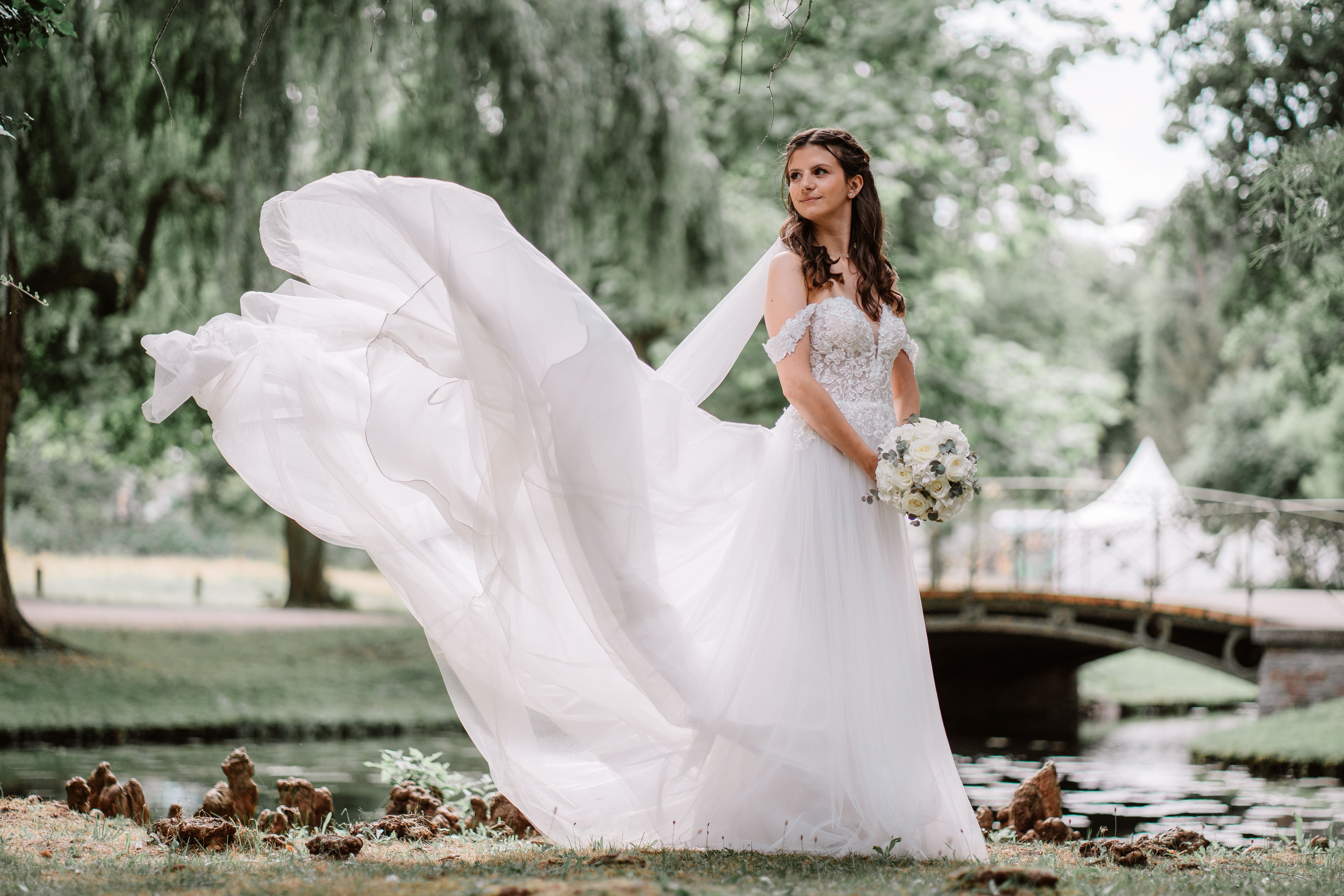 Braut im wehenden Kleid in einem Park mit Teich und Brücke