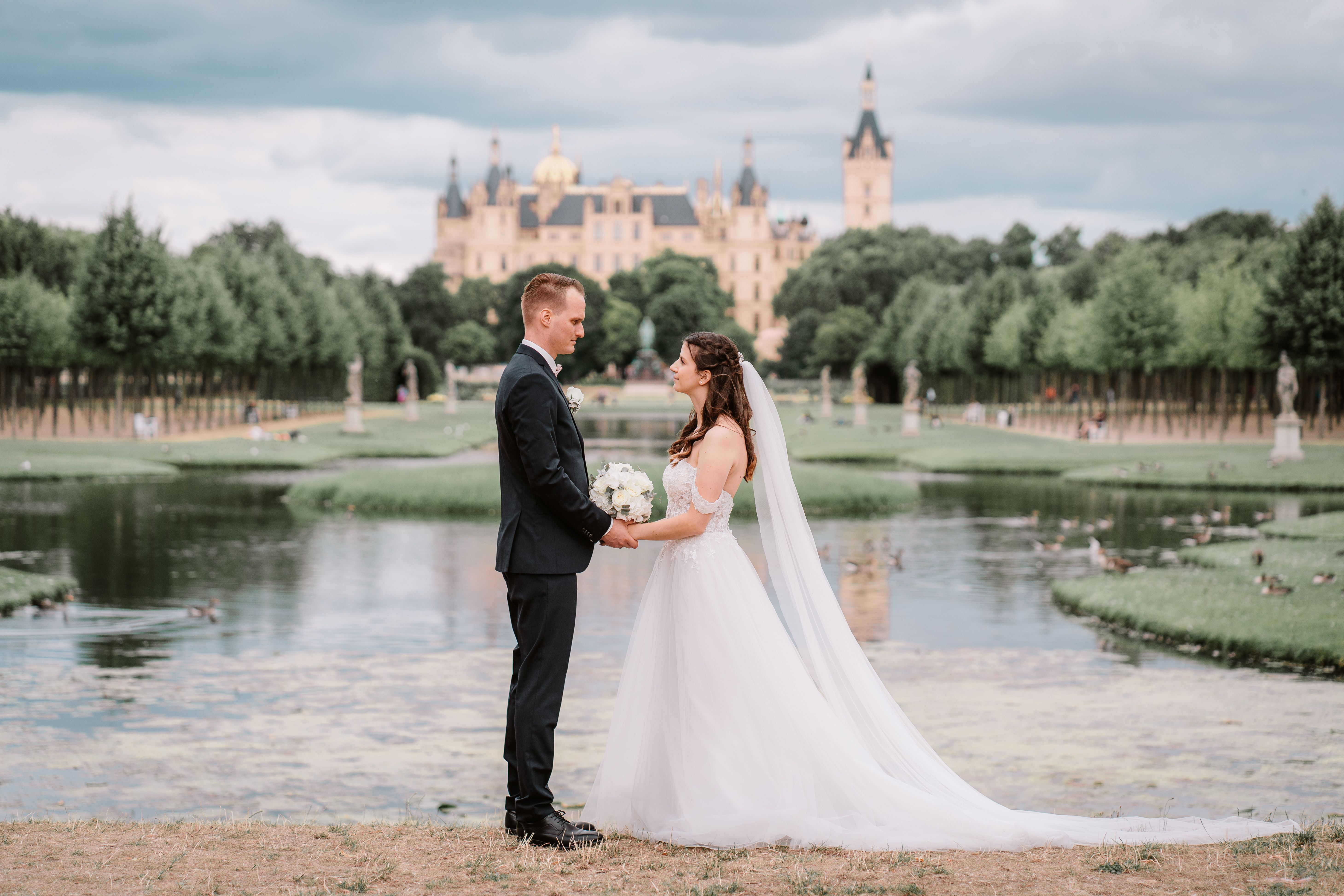 Brautpaar steht sich gegenüber an einem Wasserbecken, im Hintergrund ein Schloss