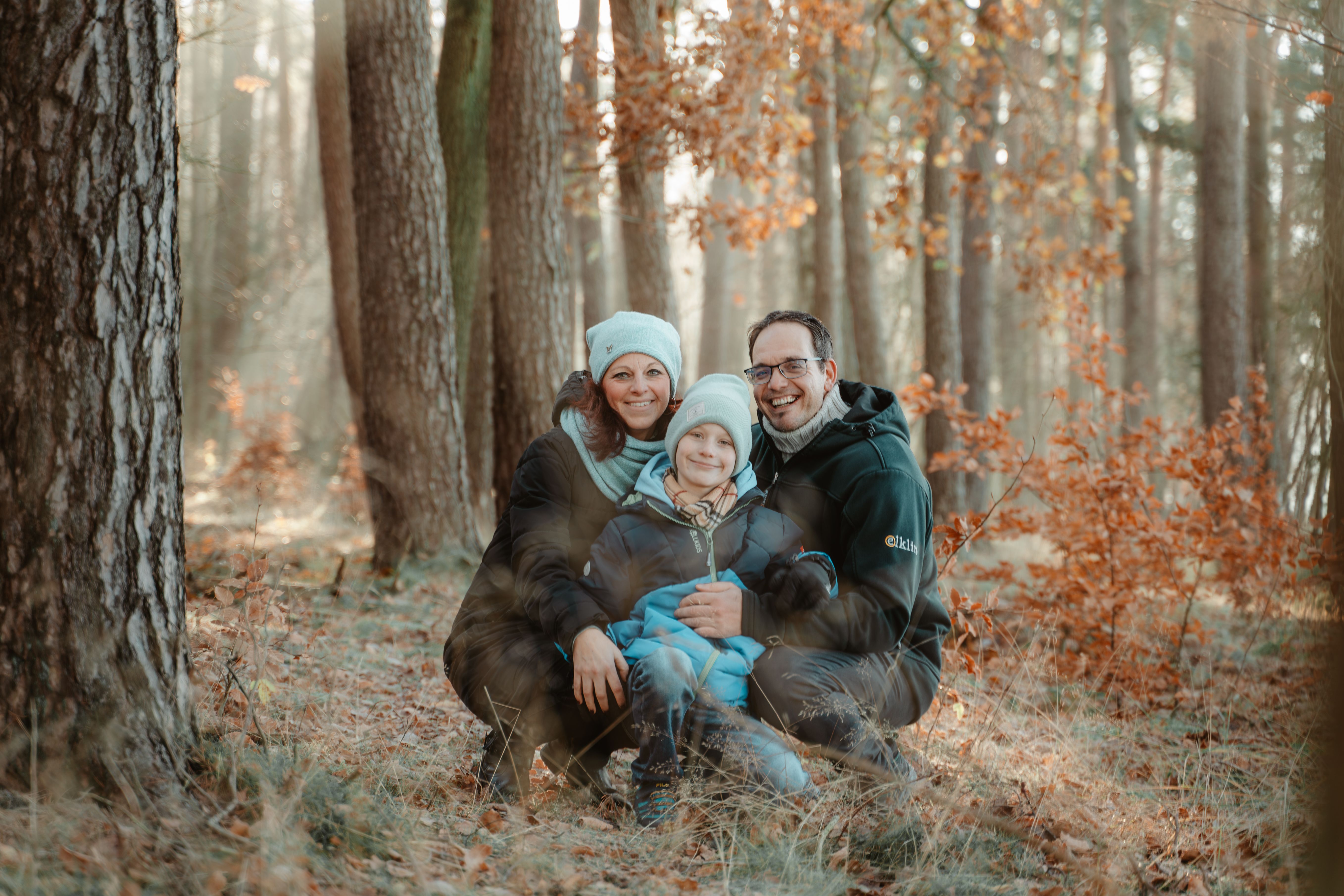 Familie sitzt im herbstlichen Wald, warmes Gegenlicht