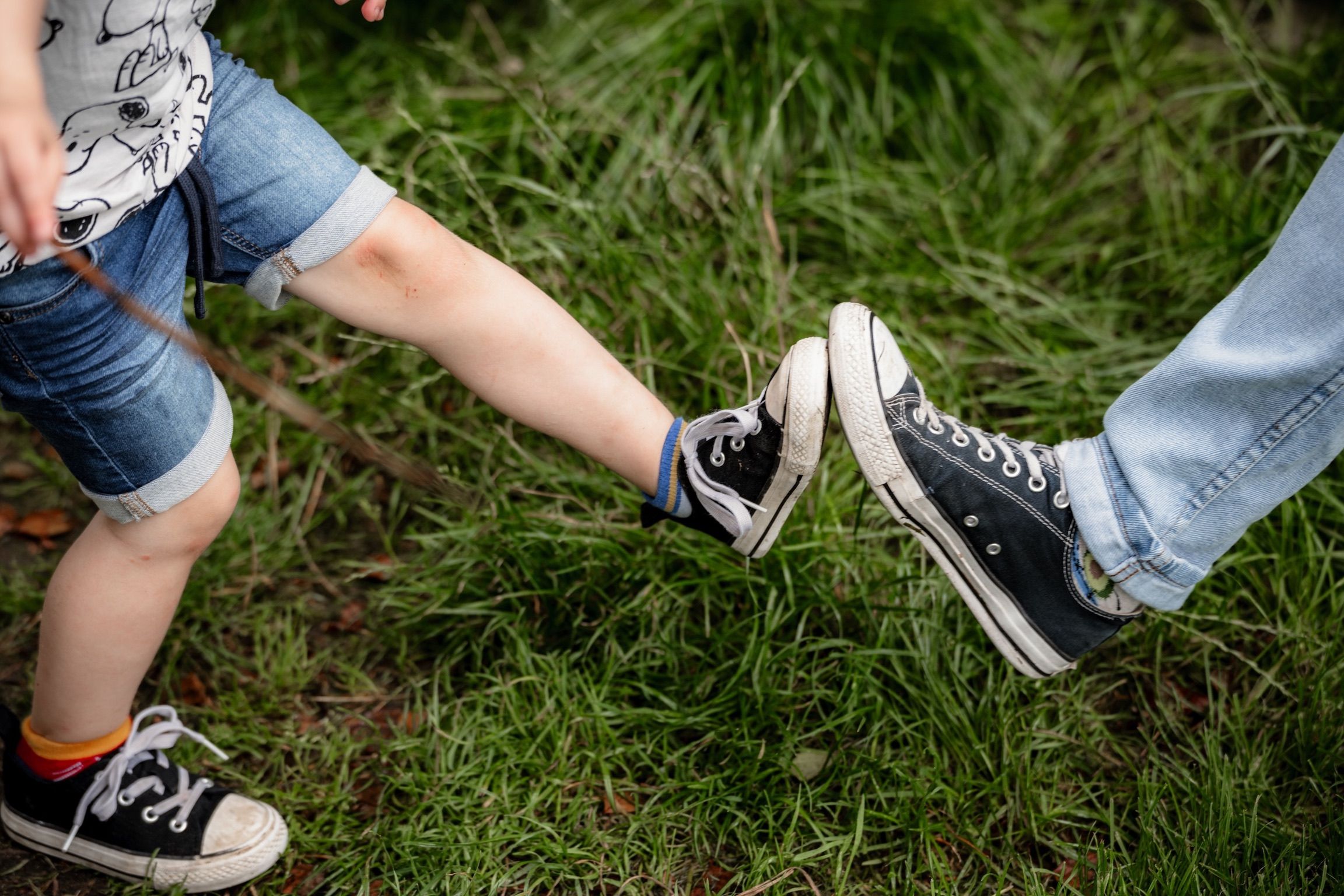 Kinderfüße und Erwachsenenfüße in Turnschuhen berühren sich im Gras