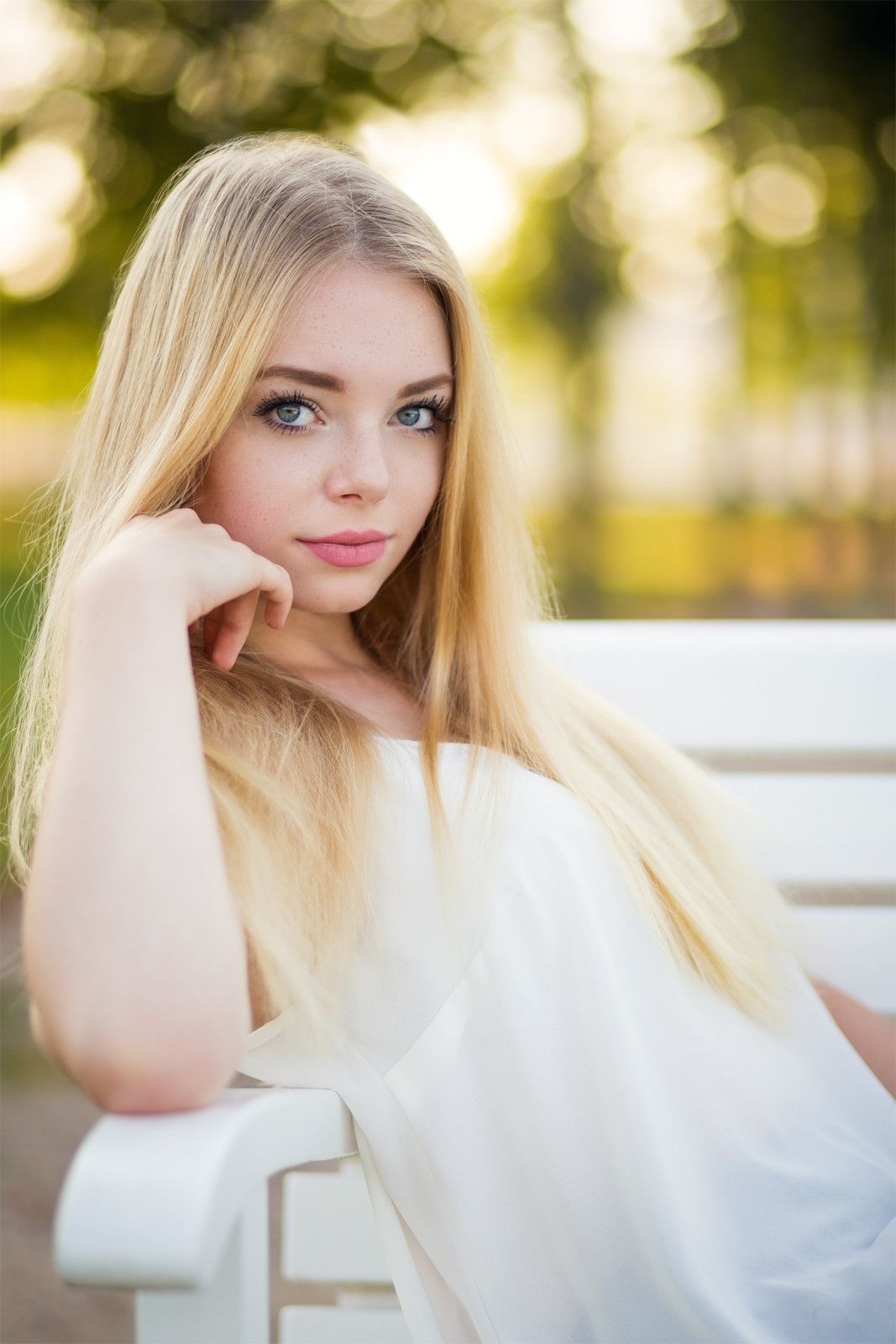 Junge Frau mit langen blonden Haaren lehnt im Gegenlicht an einer weißen Bank