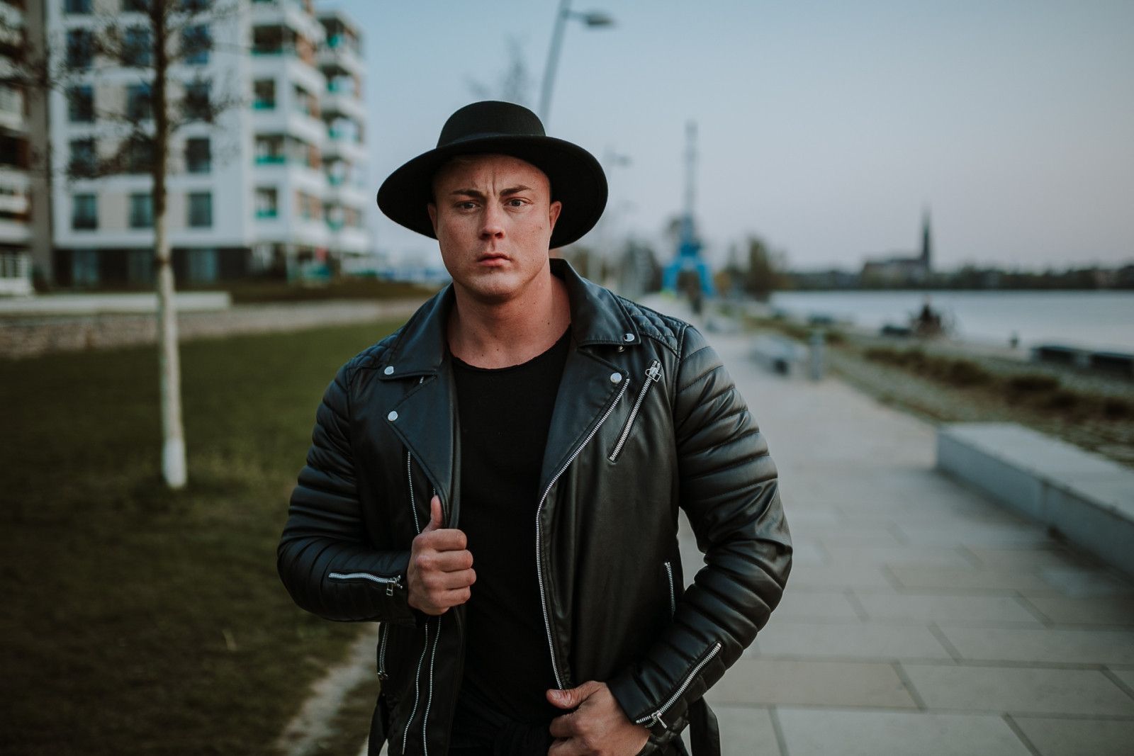 Mann mit schwarzem Hut und Lederjacke an einer Uferpromenade