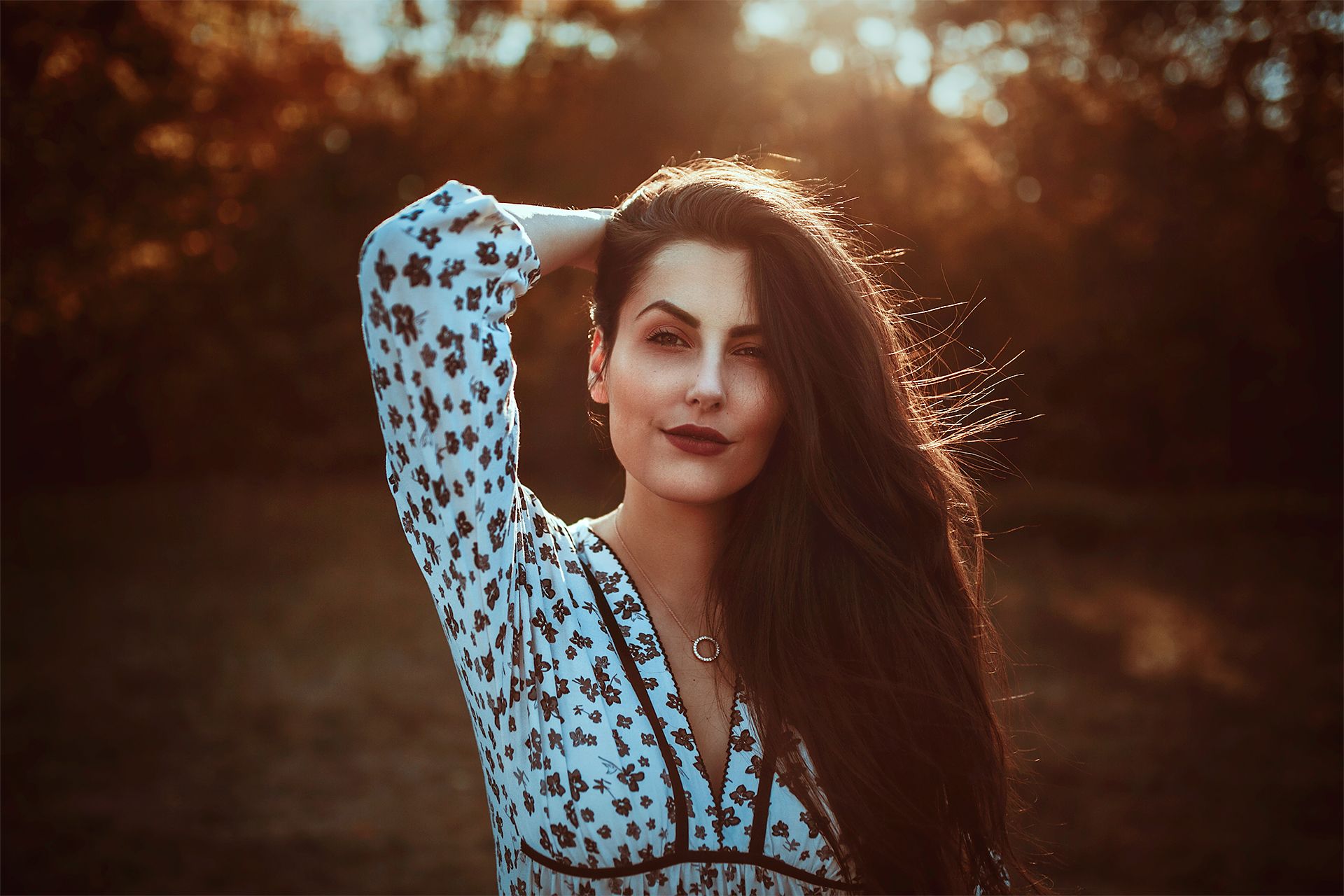 Frau mit langen dunklen Haaren im Gegenlicht der Abendsonne vor herbstlichem Laub