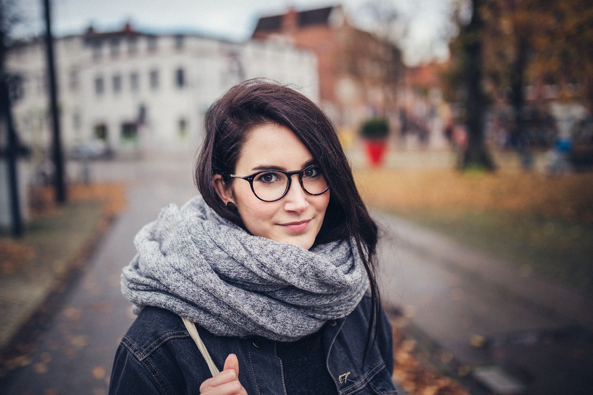 Frau mit Brille und Schal auf einer Straße im Herbst, weiches Tageslicht