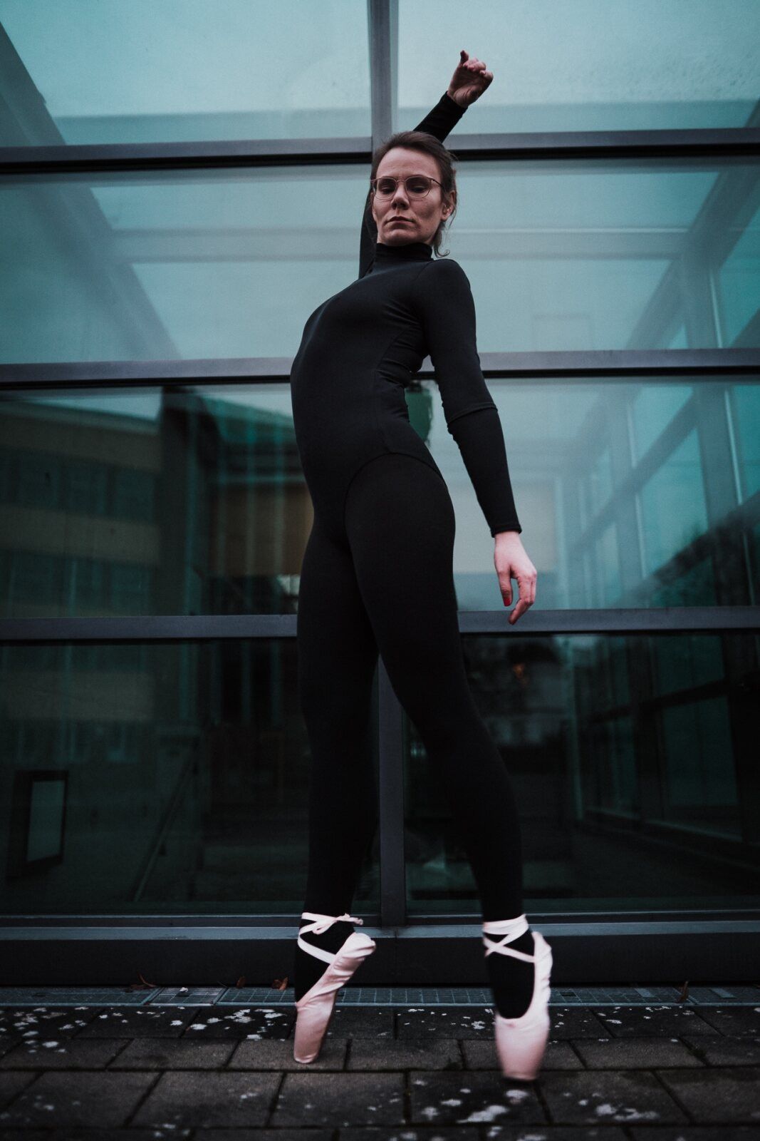 Balletttänzerin in Schwarz steht auf Spitze auf einem Glasdach