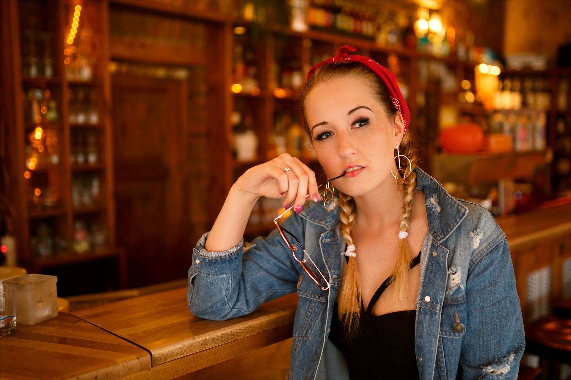 Frau in Jeansjacke lehnt an einer Holztheke in einer Bar, warmes Licht
