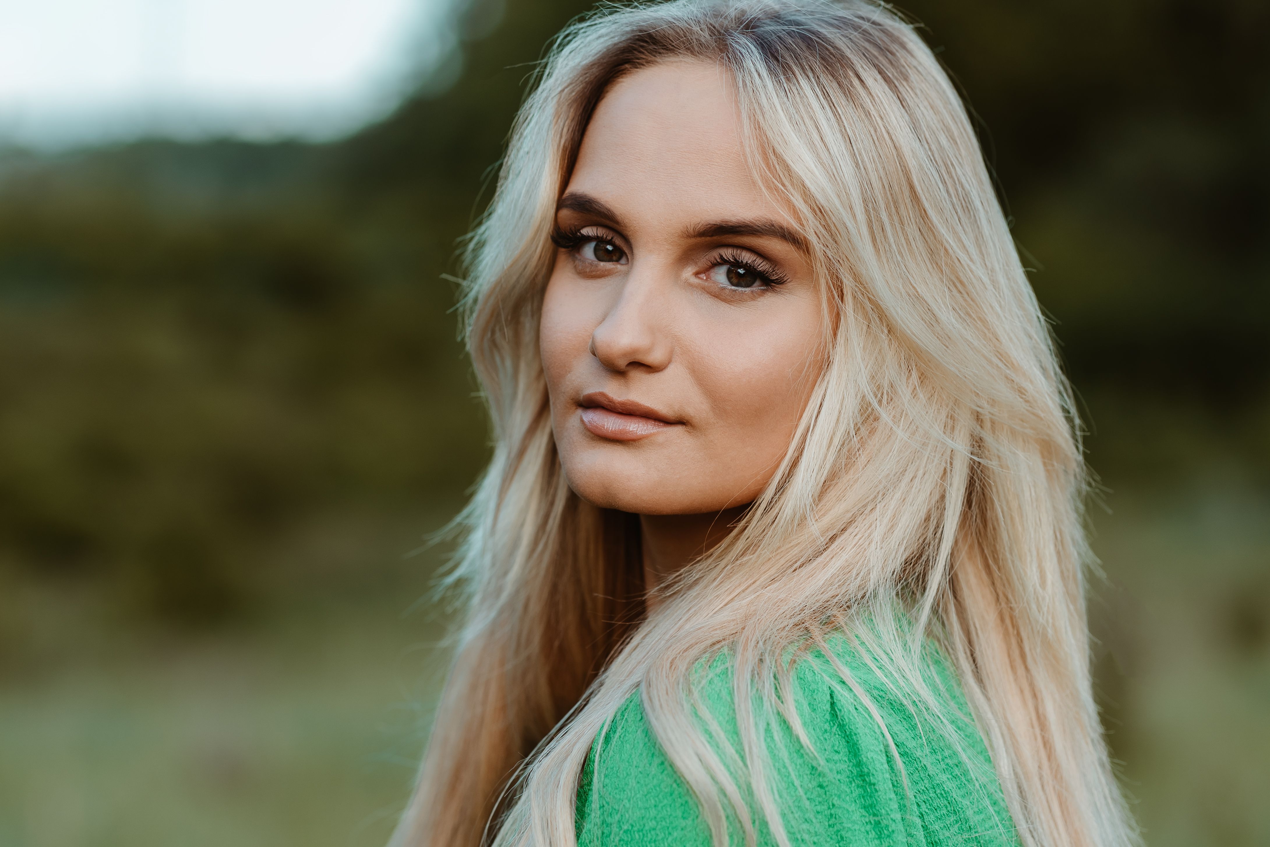 Porträt einer blonden Frau in grüner Jacke vor unscharfem Grün, weiches Licht