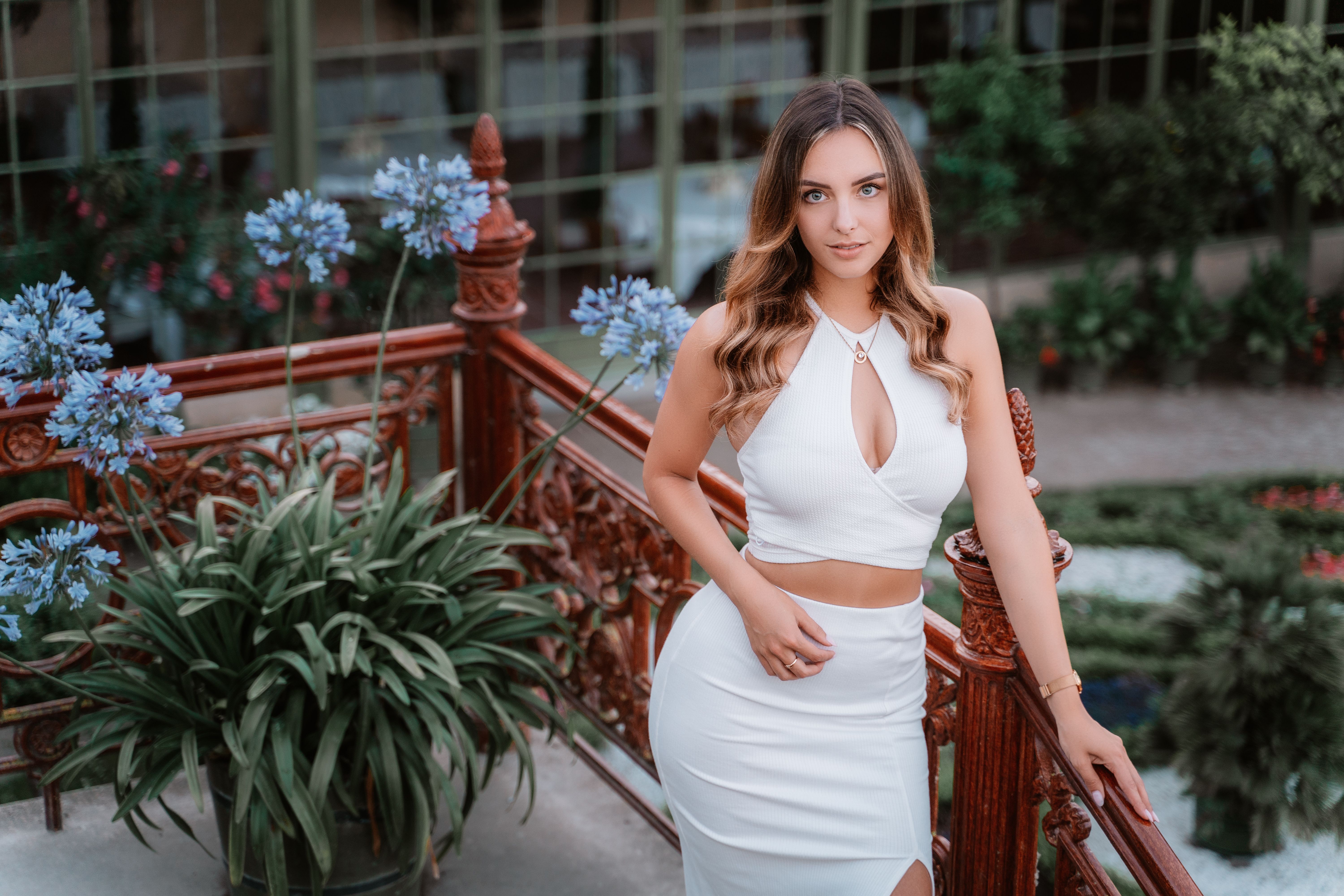 Frau im weißen Outfit auf einer Terrasse mit blauen Blumen, Tageslicht