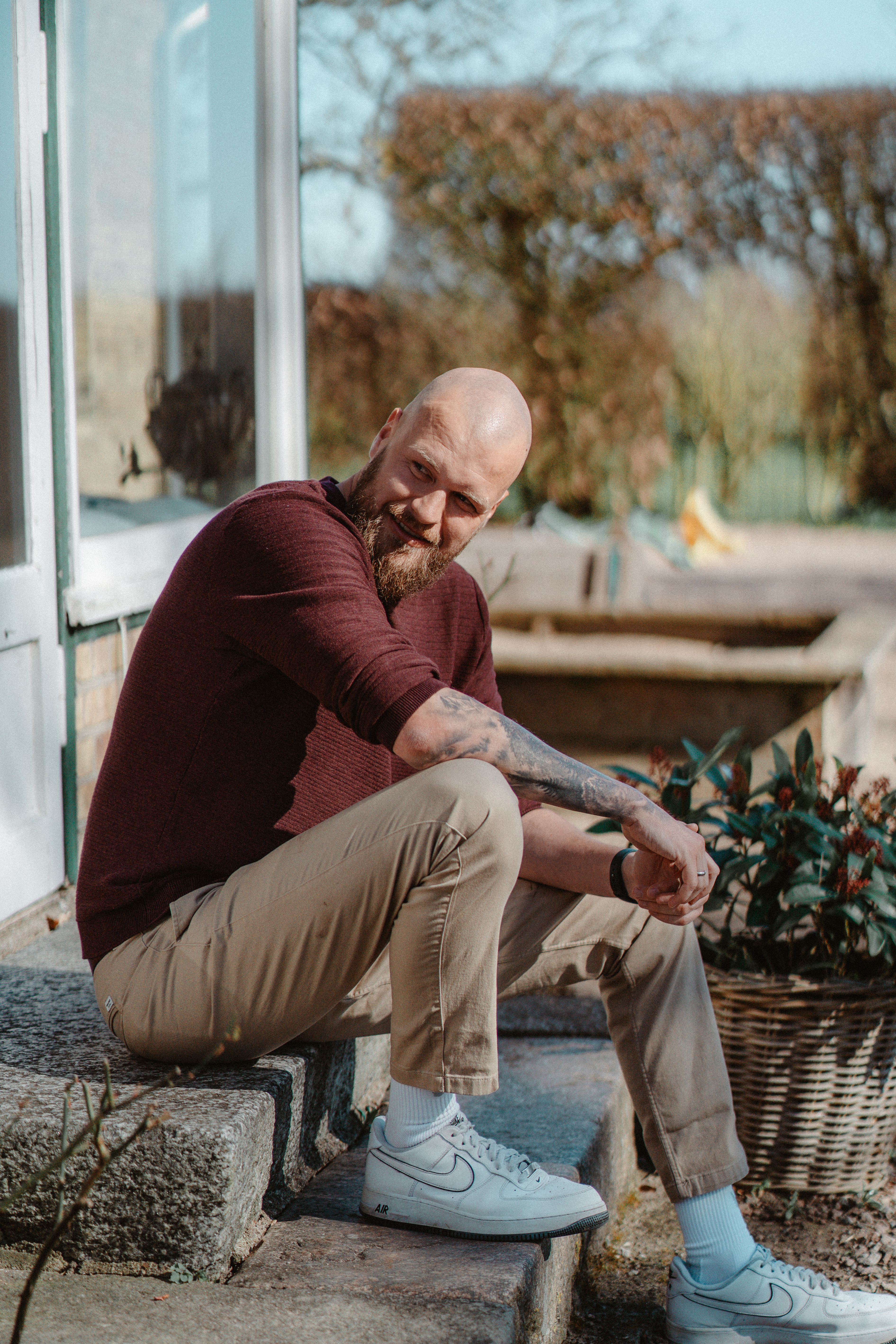 Mann mit Glatze und Bart sitzt auf Steinstufen vor einem Haus, Tageslicht